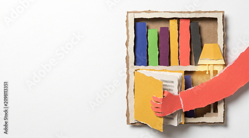 Hand reaching for a book from a colorful paper bookshelf display  