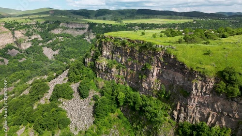 Aerial drone view of a deep river canyon surrounded by rolling green hills and rugged cliffs. Scenic natural landscape captured from above on a clear day.