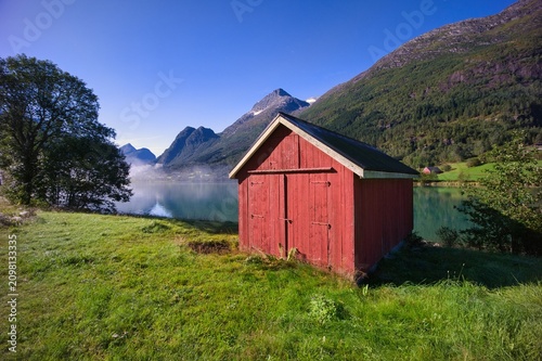 Photography Traditional red wooden boathouse on the shore of a calm scenic fjord in Norway w