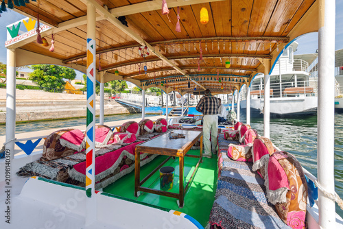 Foto An Egyptian guide and boat pilot inside a wooden felucca boat decorated ornately with colorful pillows and seats on the Nile River in Luxor Egypt
