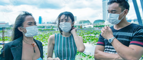 Three asian young friends standing outdoor in the city talking and wearing face masks in covid coronavirus pandemic