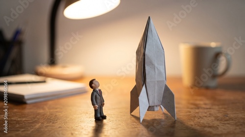 Origami rocket ship with a miniature businessman standing beside it, ready for a new venture or innovation