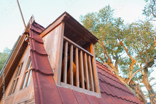 Photos A rustic wooden dormer window on a red tiled roof with leafy trees in the background