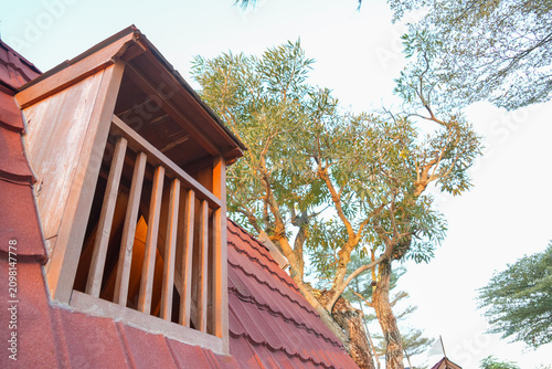 Photos A rustic wooden dormer window on a red tiled roof with leafy trees in the background