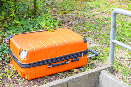 фотографія Orange suitcase with hole on ground, greenery, outdoor abandoned luggage, travel