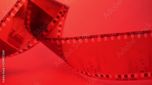35mm negative photographic film in rotation in red room, camera darkroom. Slightly rolled film strip isolated on red background. Analog film strips. Analog photography.