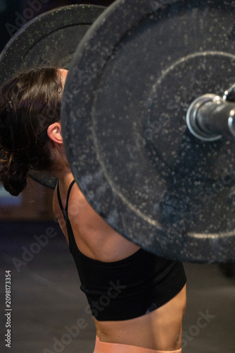 Focused Woman Performs Overhead Press Workout, Determined Female Weightlifter Executes Overhead Lift Amidst Gym Dust, Confident Woman Athlete Concentrates During Intense Overhead Push In Gym