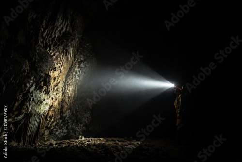 A single beam of light from a helmet lamp illuminates a dark cave.