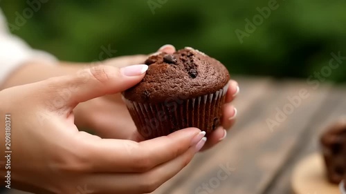 Close-up hands holding a delicious chocolate muffin, highlighting its rich texture and tempting sweet appeal. A delightful baked treat for an indulgent moment outdoors
