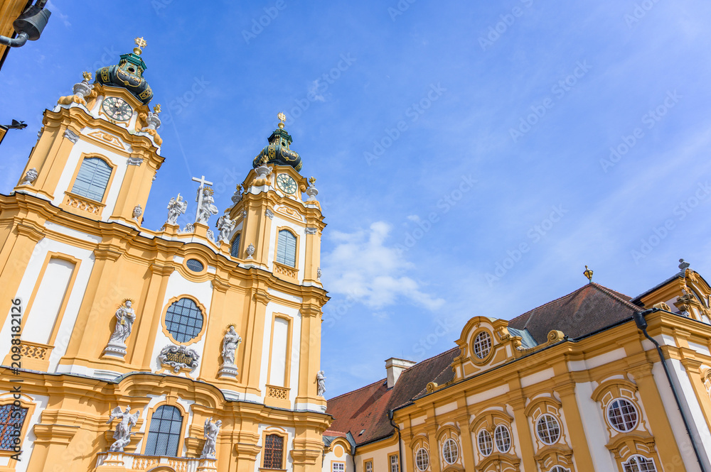 Obraz premium Melk Abbey stands majestically against a bright blue sky showcasing its baroque architecture with intricate details and striking stained glass windows, its towering green domes