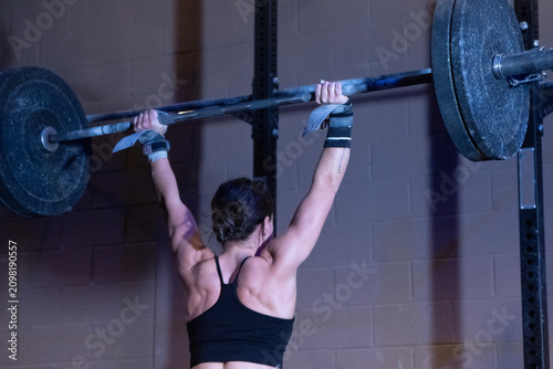 Woman lifting weights weightlifting, in gym, with barbell, weights, from a side view perspective, with black, gray accents, and determined mood, with nearby objects.