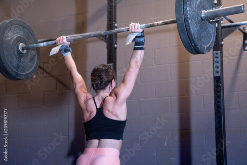 female weightlifter performing clean and jerk lift in gym environment with rubber weights and metal barbell, rear view, determined and focused, black and pink attire, fitness and strength.
