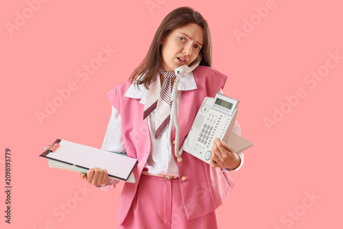 Bild auf Leinwand Confused young businesswoman holding a landline phone and clipboard, multitaskin