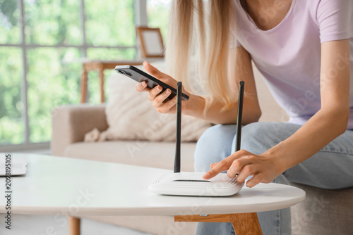 Obraz na plátně Woman setting up a wireless router with a smartphone for home internet connectio