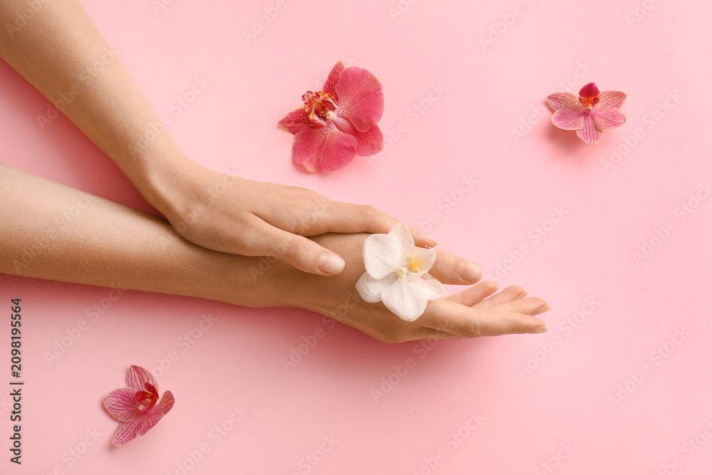 Obraz premium Female hands with delicate white orchid flower on a soft pink background, beauty and skincare