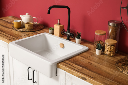 White counters with houseplants  teapot and cups near red wall in interior of modern kitchen  closeup