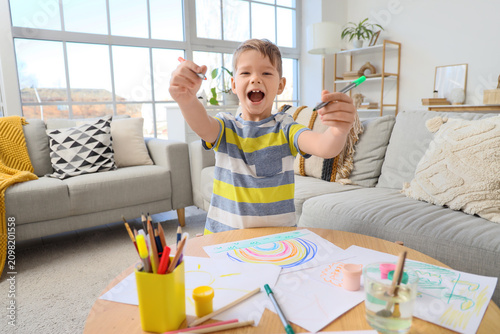 Happy little boy with felt-tip pens drawing at home