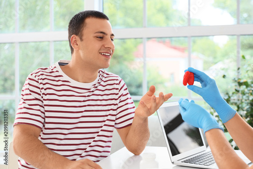 Female endocrinologist showing thyroid gland model to man in clinic