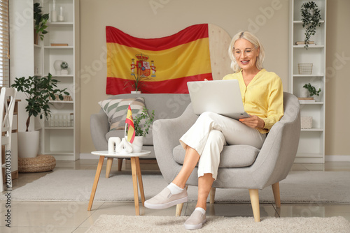 Mature woman with laptop learning Spanish online in armchair at home