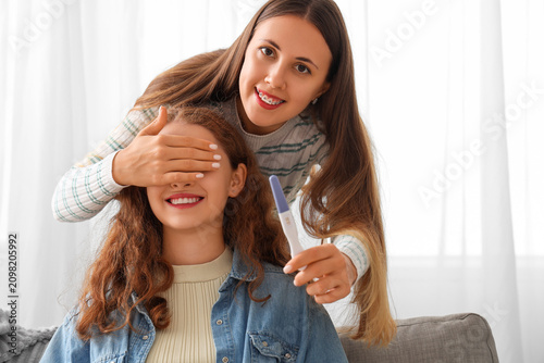 Young lesbian woman with pregnancy test covering her wifes eyes at home