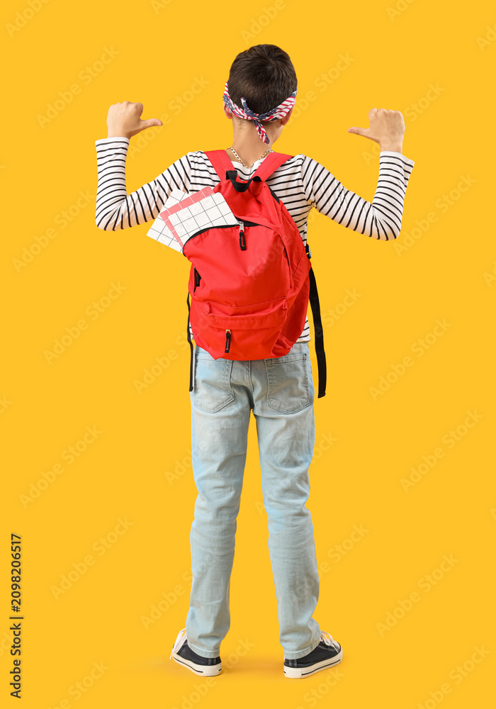 Naklejka premium Schoolboy pointing at red backpack on orange background, back view