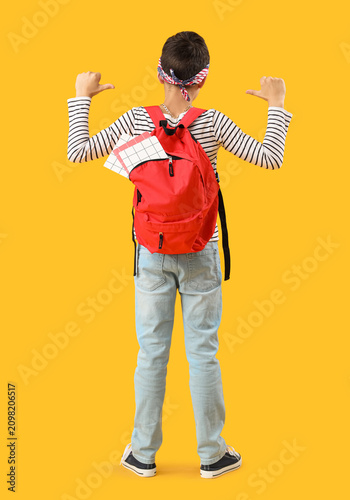Schoolboy pointing at red backpack on orange background  back view