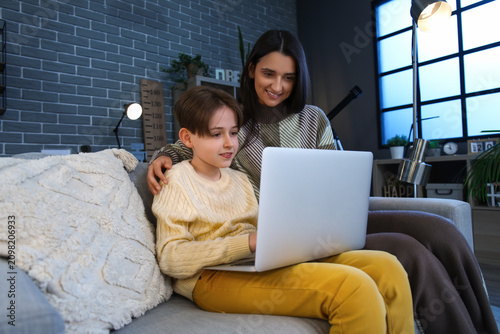Little boy and his mother doing homework with laptop at home late in evening