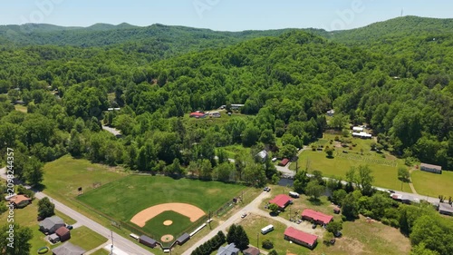 Aerial perspective of Rosman, North Carolina, highlighting a baseball field with surrounding homes and dense green trees in a tranquil rural landscape