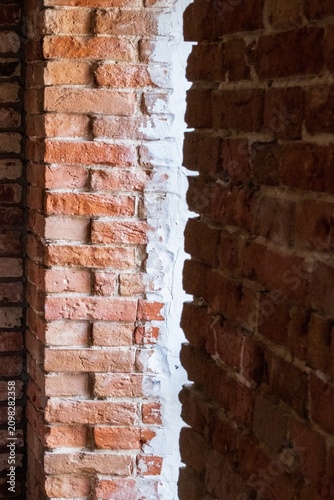 A close-up of a weathered red brick wall with a jagged, partially peeled white coating, creating a stark vertical contrast between the textured masonry and the bright painted edge