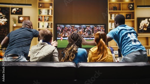 Football supporters argue over a referee decision at home, shouting and raising hands as frantic soccer fans react to a dramatic live game on TV.