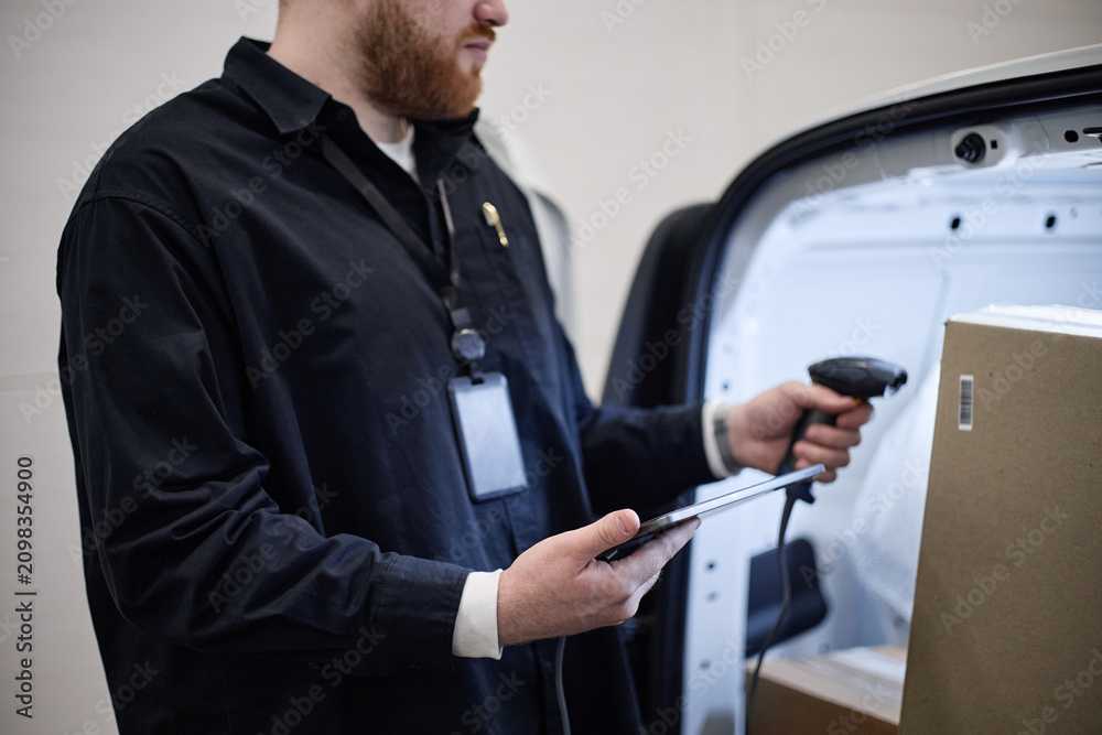 Fototapeta premium Caucasian young adult delivery worker scanning package barcode with handheld reader and checking tablet at van, managing individual storage logistics. For shipping, inventory, fulfillment marketing