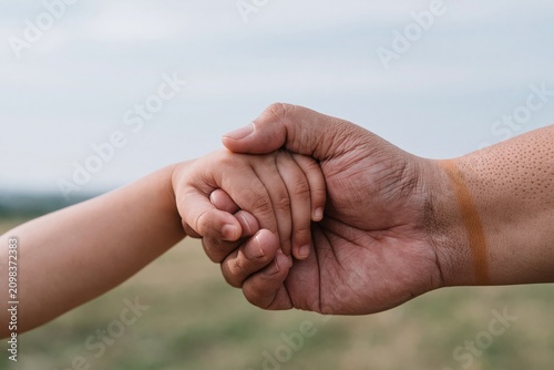 Adult hand gently holding a childs hand in a protective clasp against a soft hazy blue horizon for family lifestyle and insurance advertising