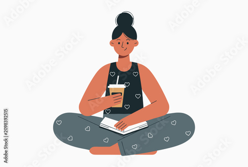 Young woman sits comfortably cross-legged on the floor while reading an open book and holding a cup of hot coffee.