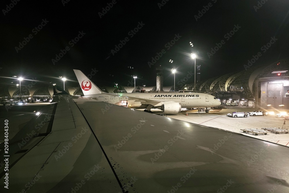 Obraz premium Hong Kong, China - July 01, 2026: Japan Airlines airplane at airport terminal at night viewed from airplane wing.