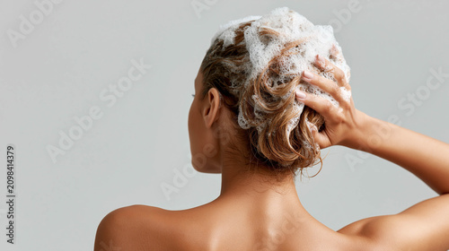 Back view of a woman washing her hair with soapy shampoo foam, clean female showering and lathering hair, haircare or head spa concept.
