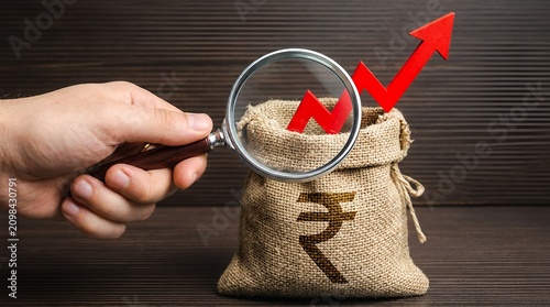 Indian rupee money bag with rising red arrow, hand holding magnifying glass analyzing financial growth, investment and inflation concept