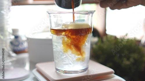 4K Close-up barista pouring hot espresso shot into plastic glass filled with ice and coconut water, Cafe beverage menus coffee shop marketing.