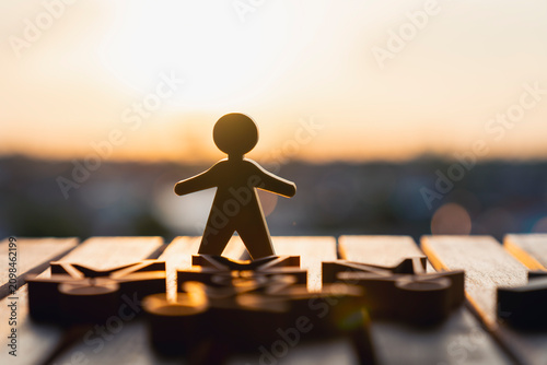 Fotografie Wooden human figure standing outstandingly over lying figures at sunset
