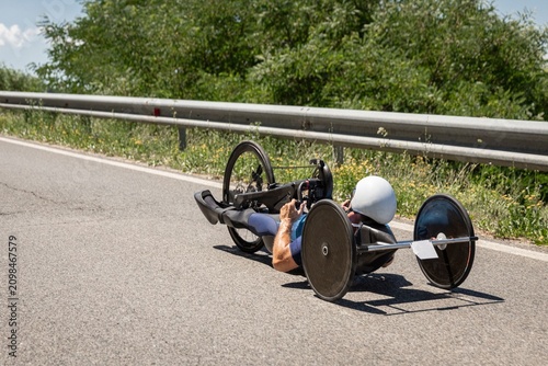 Paracyclist racing on a handcycle during a road cycling competition on a closed mountain road. The athlete speeds toward the finish under bright summer sunshine, showcasing determination, endurance