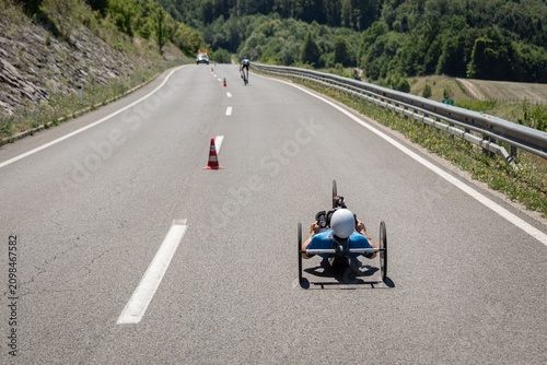 Paracyclist racing on a handcycle during a road cycling competition on a closed mountain road. The athlete speeds toward the finish under bright summer sunshine, showcasing determination, endurance
