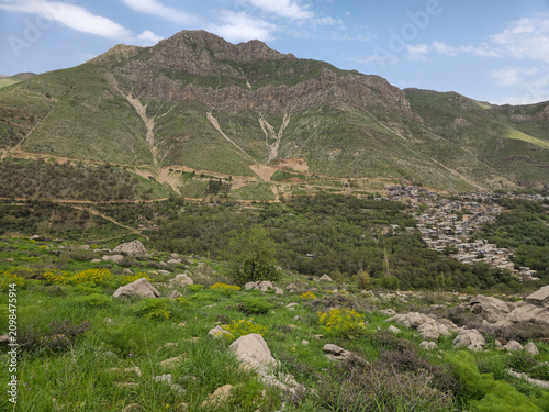 Spring mountain landscape overlooking a rural village with green meadows, rocky hillsides, wildflowers, and forest beneath a partly cloudy sky.
📍 Kamalla village, Hawraman Takht, Kurdistan 