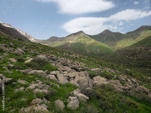 Rocky boulders and green grass cover a mountain hillside overlooking layered spring peaks with patches of snow in the distance.
📍 Hawraman Takht, Kurdistan, Iran 