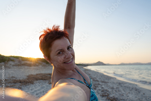 Bild auf Leinwand Senior woman smiling taking selfie on beach at sunset
