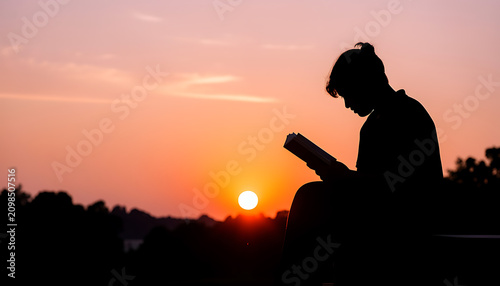 Silhouette of a man reading a book outdoors at sunset