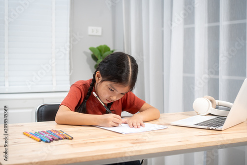 Tableau sur toile Young girl doing homework and writing in a notebook at a desk with a laptop and