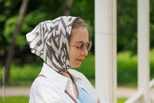 Obraz na plátne Woman in sunglasses and scarf enjoys a sunny day in a picturesque park