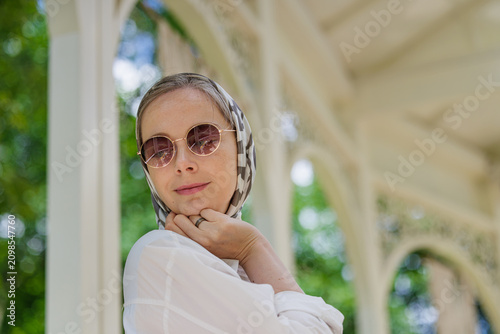 Bild auf Leinwand Charming woman wearing a stylish scarf and round sunglasses in a lush garden set