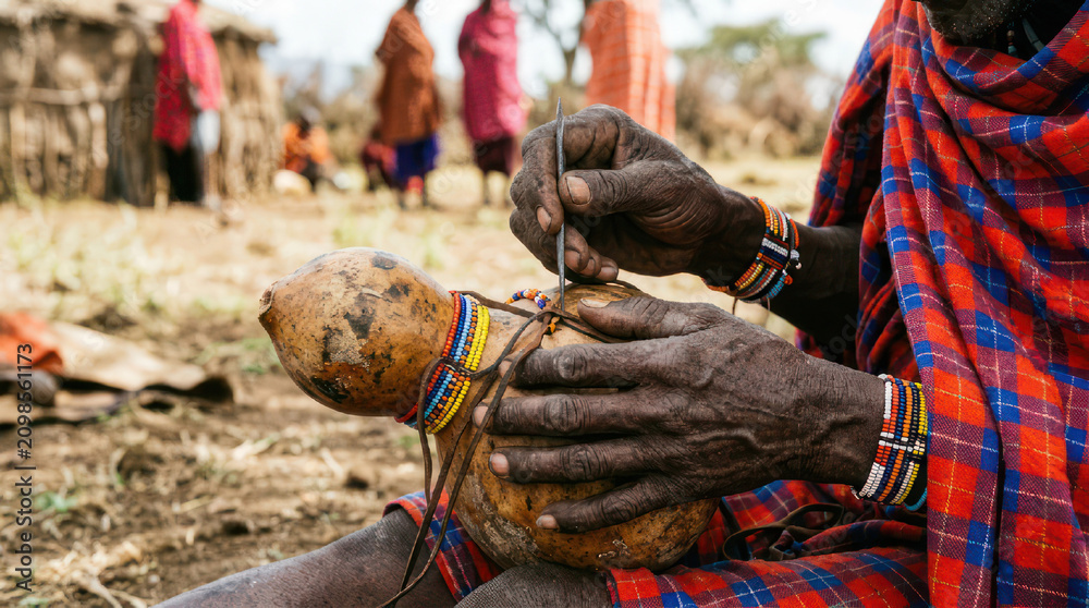Obraz premium Maasai man crafting traditional gourd with beads and tools.