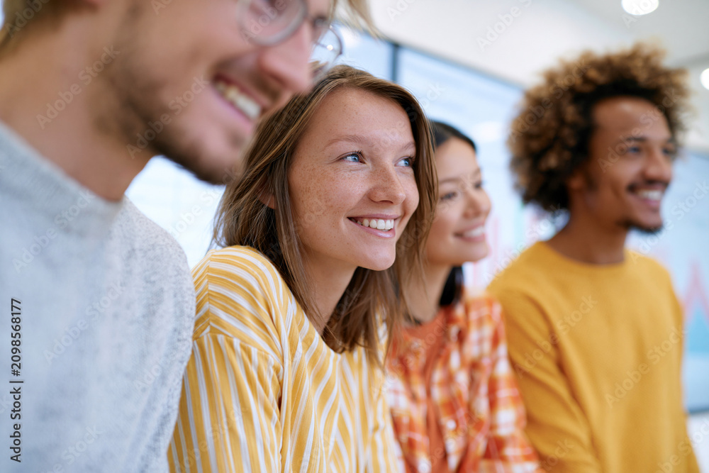 Obraz premium Young adults smile brightly in a casual group setting. Their expressions show warmth and joyful engagement. The scene suggests collaborative learning or creative teamwork