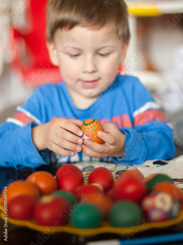 Child's gentle hands cradle a brightly painted Easter egg, surrounded by an array of colorful festive eggs on a golden tray indoors